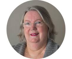 Margaret Ogden, with shoulder length hair and wearing glasses and lipstick, smiling at the camera. 